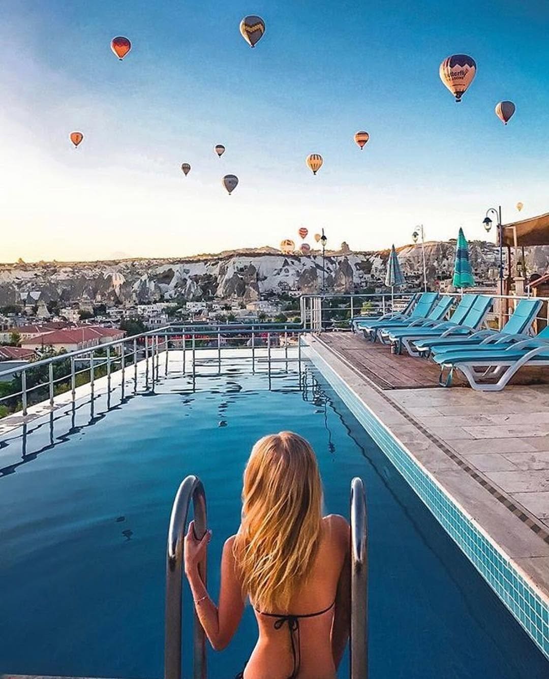 Doors of Cappadocia'nın çatı havuzunda gün doğumunda Göreme üzerinde yükselen sıcak hava balonları