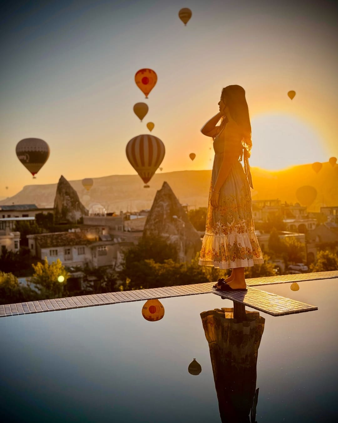 Doors of Cappadocia'nın çatı terasında gün doğumunda silüet halinde bir misafir, arkasında sıcak hava balonları ve Kapadokya'nın peri bacaları