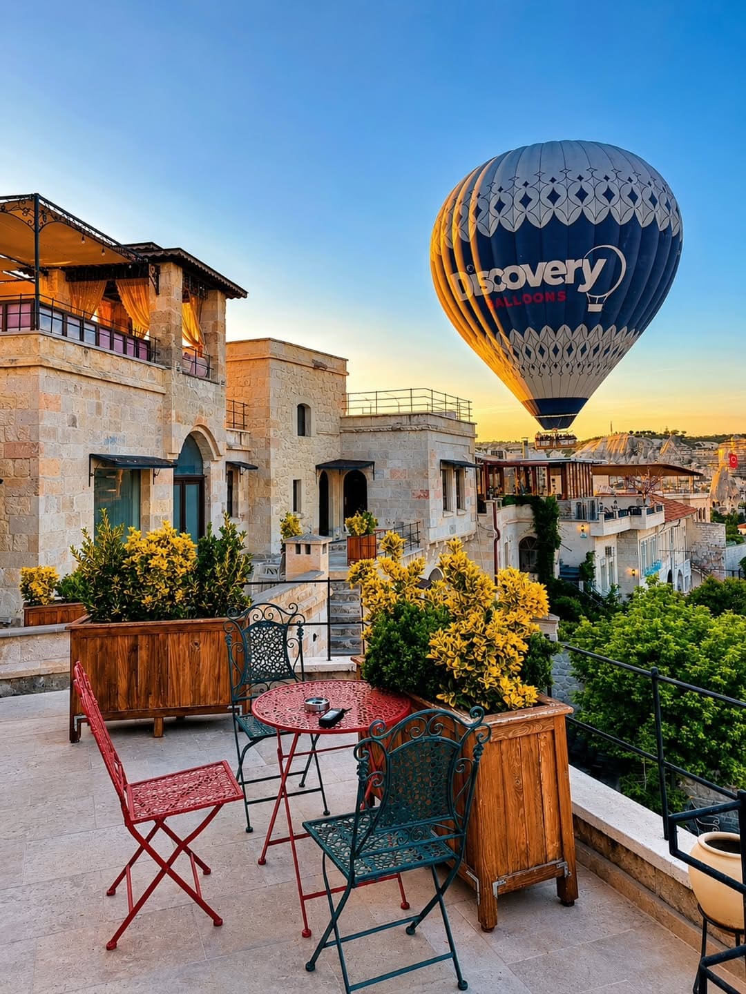 Doors of Cappadocia'nın çatı terasında kahve sandalyeleri ve gün doğumunda Göreme üzerinden geçen bir sıcak hava balonu