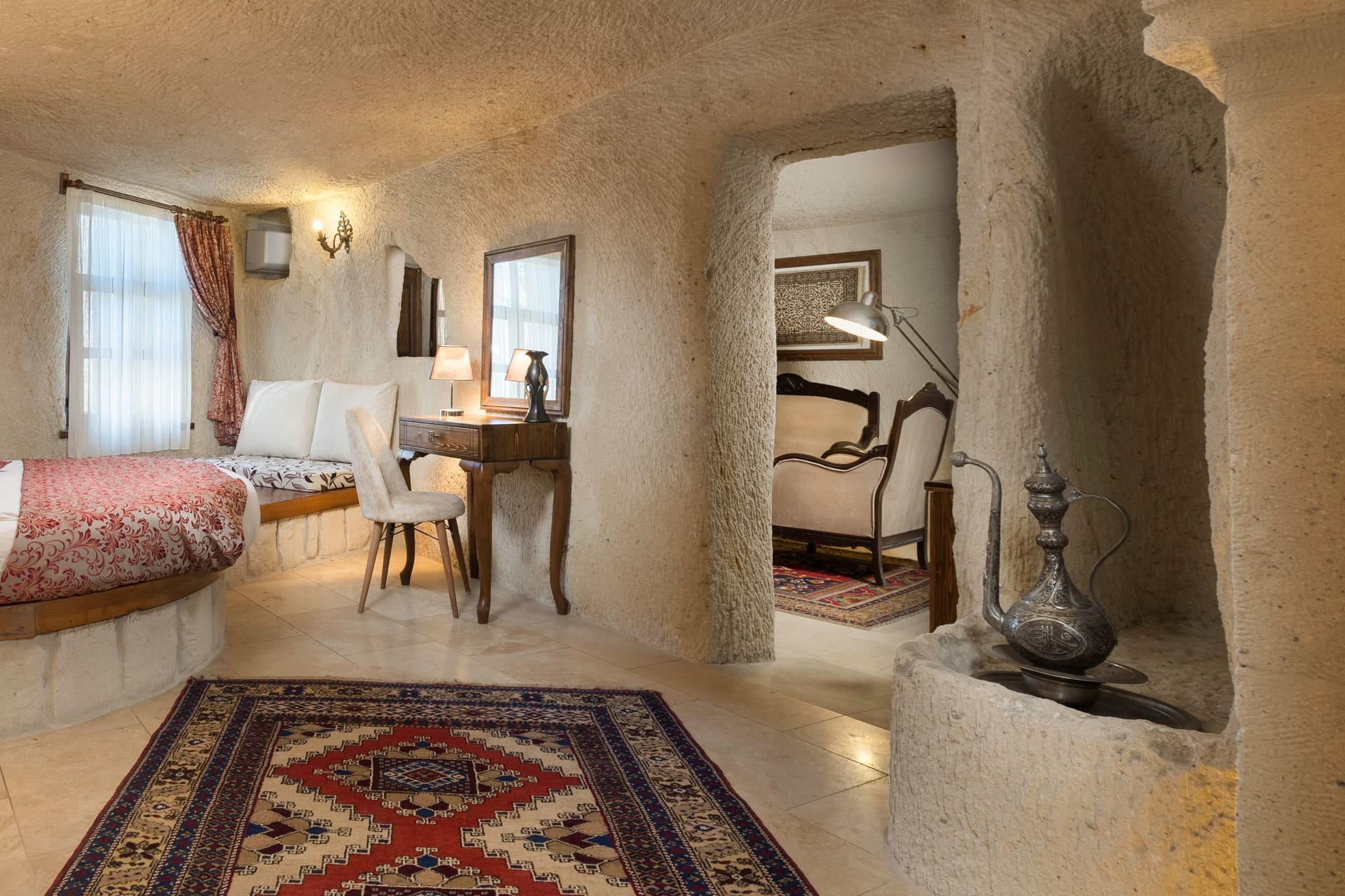 Room 112, King Cave Suite: wide view of the room with the bed, a mirrored dressing table, and an arch to a small seating alcove