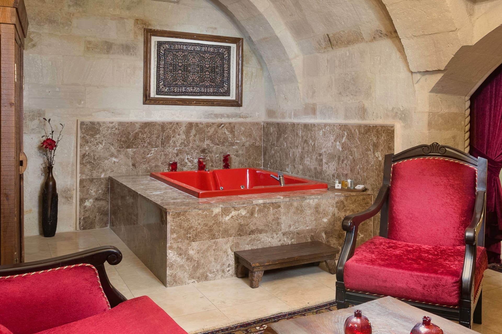 Room 110, Queen Suite: A red jacuzzi tub in a stone-tiled corner, an armchair beside it.
