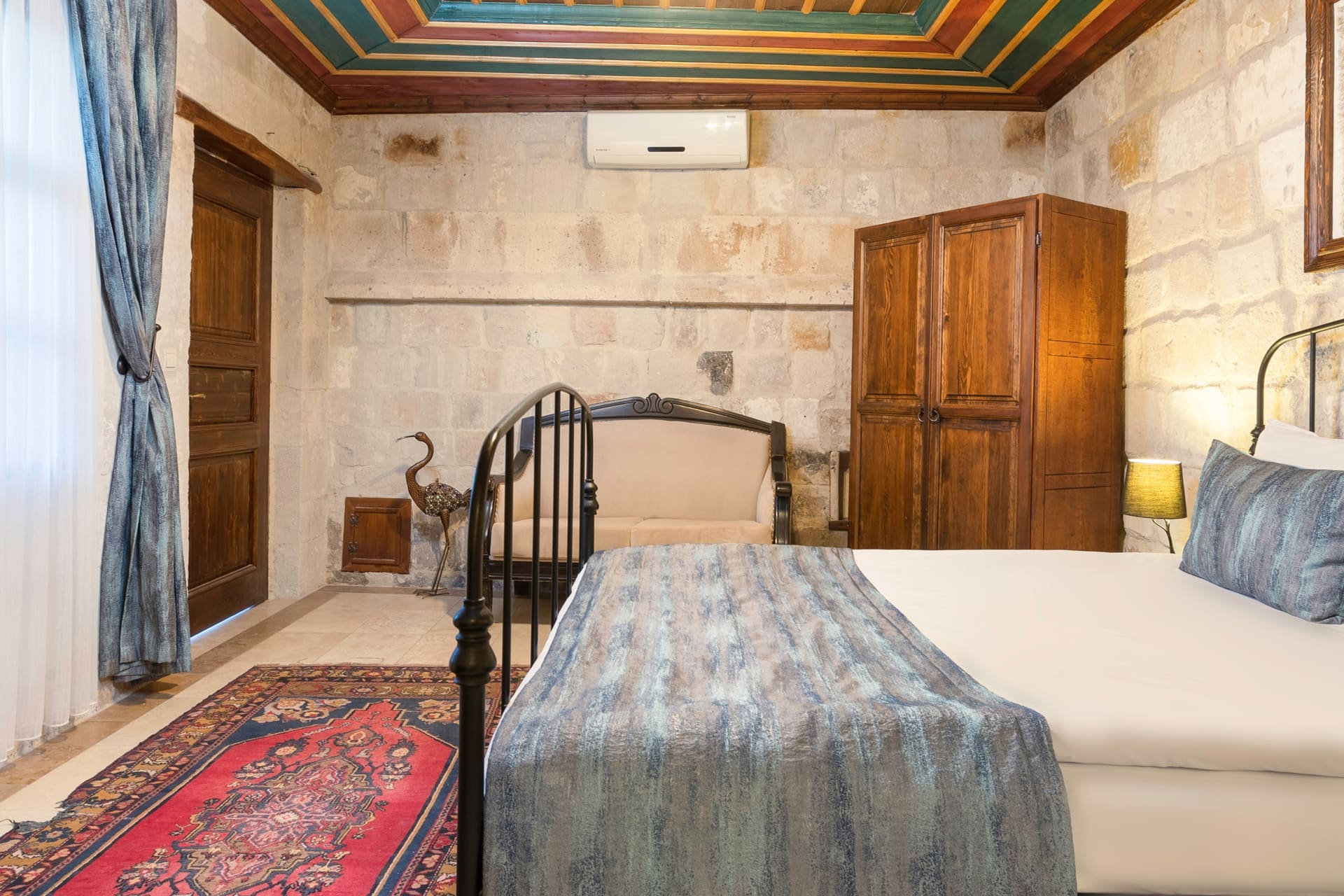 Room 101, Deluxe: View from the bed toward the door, stone walls, air conditioning unit, painted ceiling