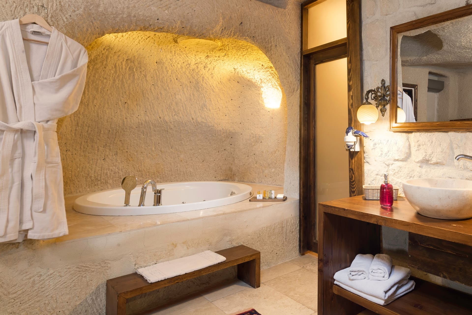 Room 113, Junior Cave Suite: oval bathtub in a stone alcove, hanging robe, sink behind