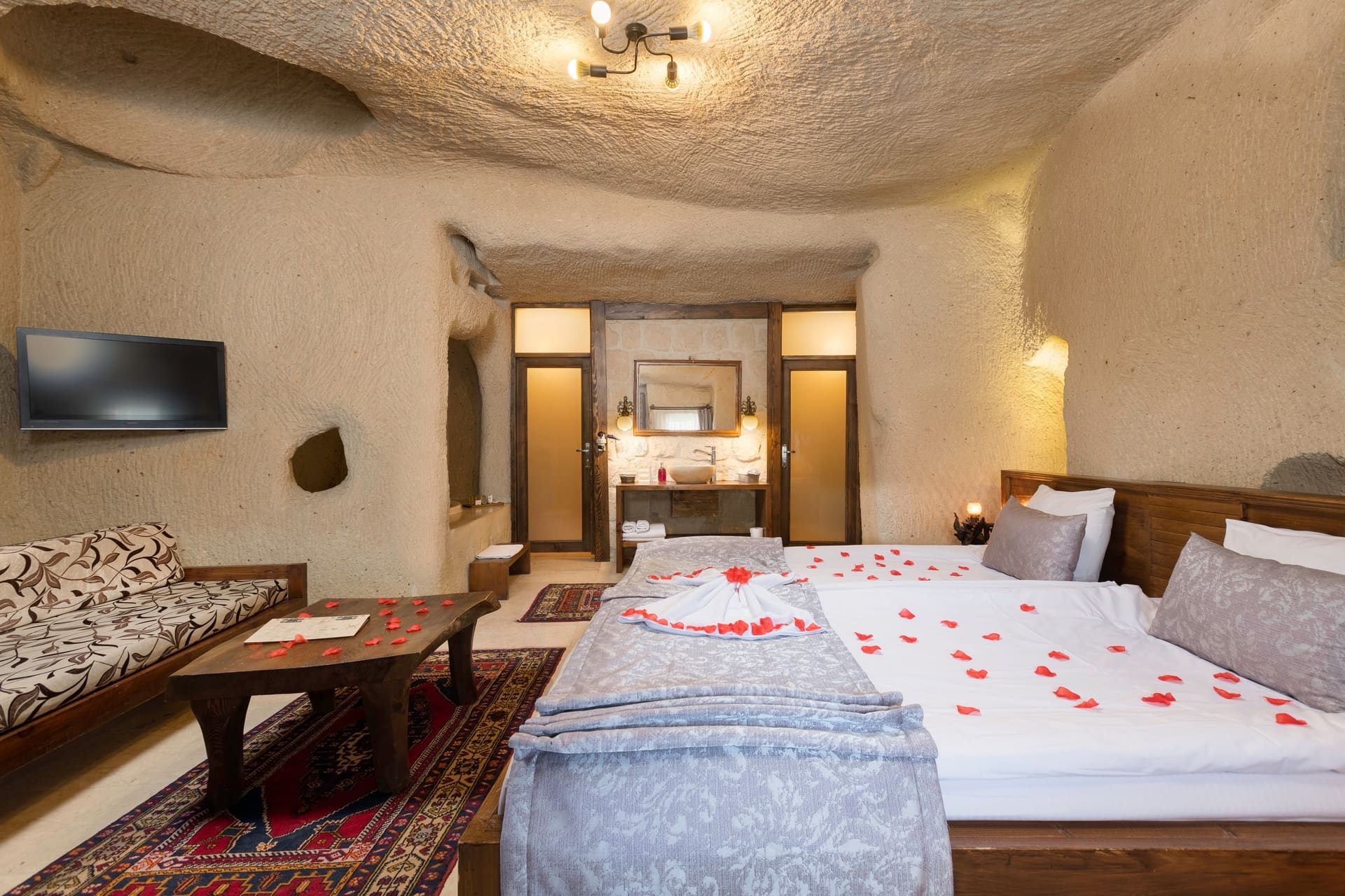 Room 113, Junior Cave Suite: room seen from the entrance, wall TV, mirrored console, rose petals on the bed