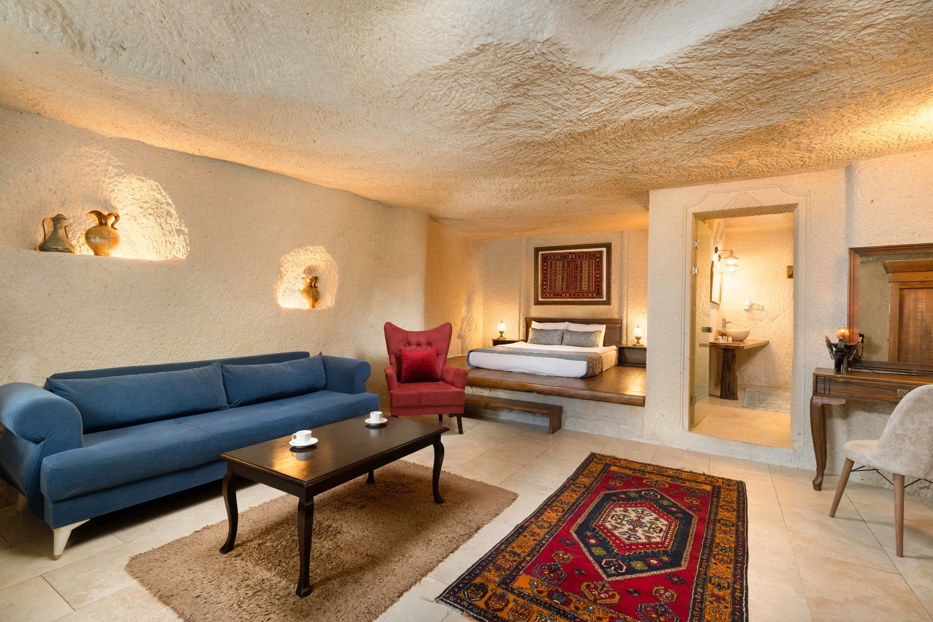 Room 114, Junior Cave Suite: living area with a blue sofa, burgundy armchair, bed alcove behind