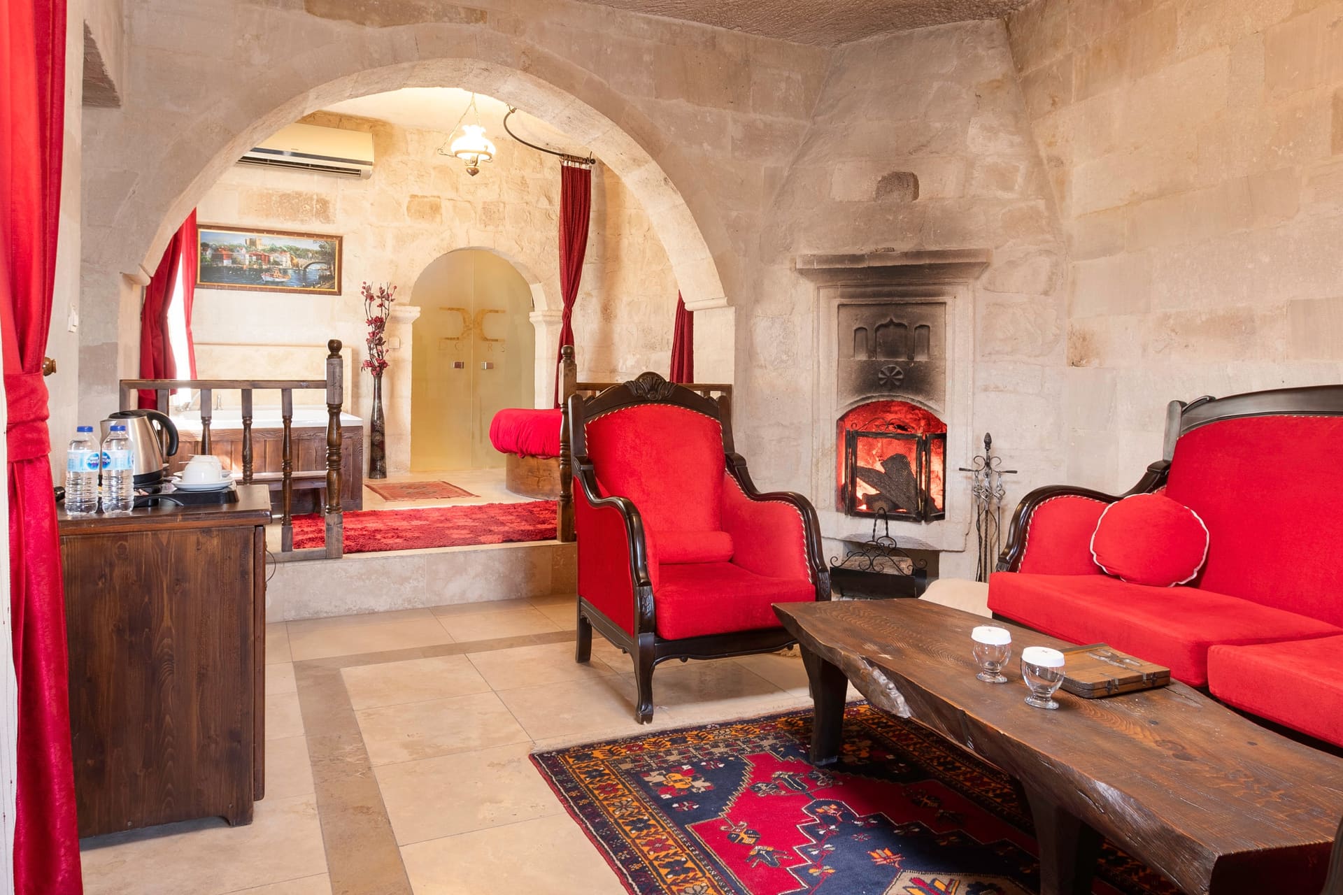 Room 107, King Suite: the bed with a red cover, an armchair and the passage to the hallway