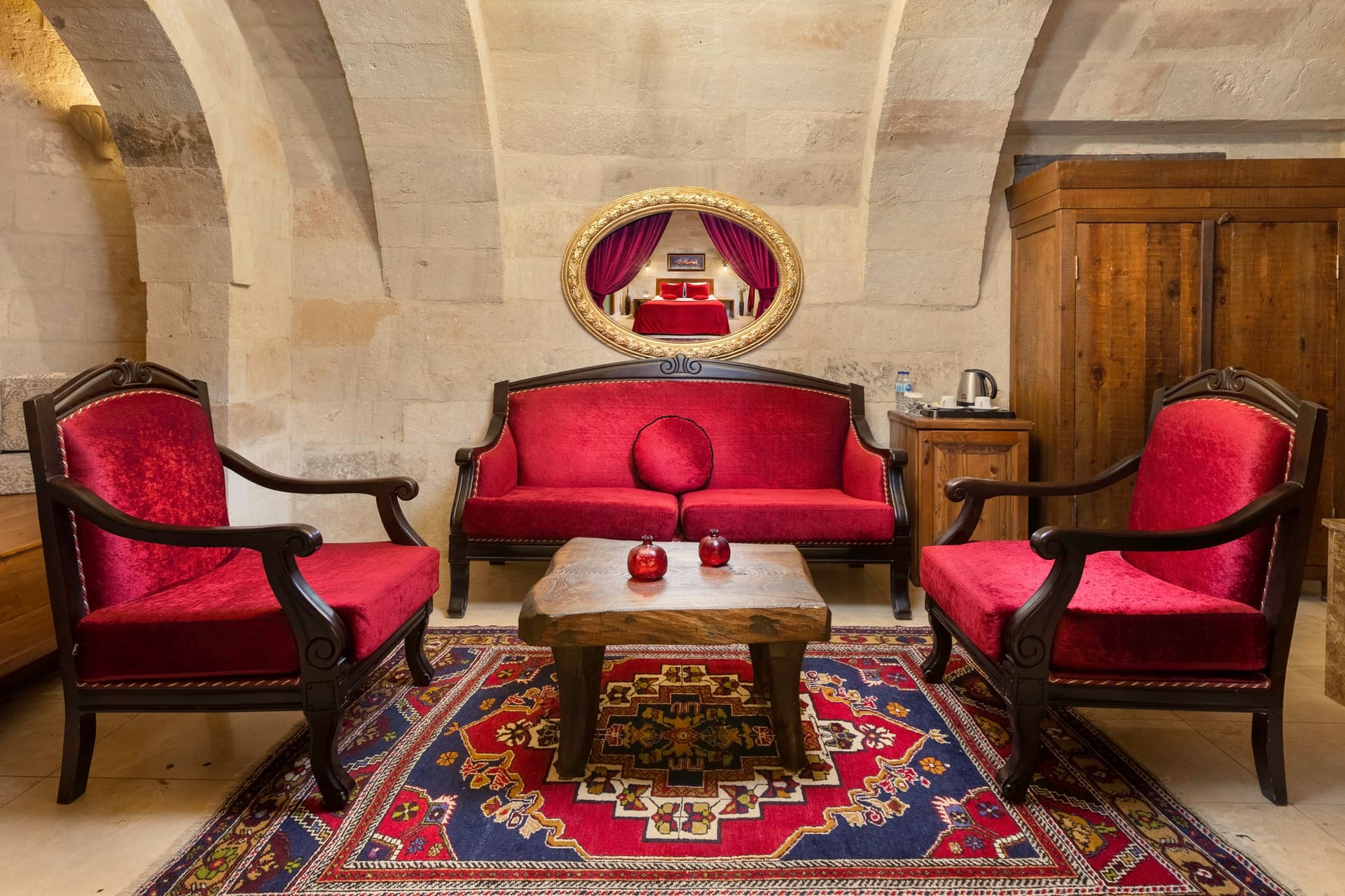 Room 110, Queen Suite: A larger seating area with a red sofa and armchairs, chandelier on the vaulted ceiling.