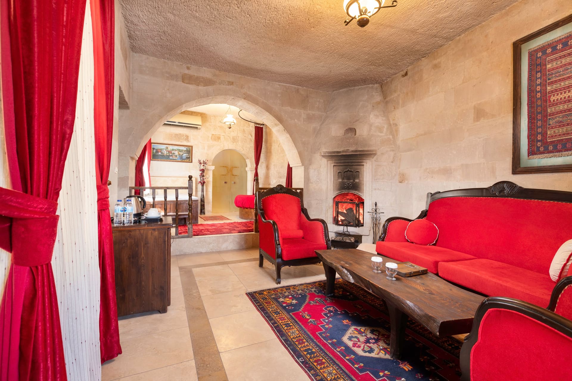 Room 107, King Suite: view through the stone arch into the seating area with a red armchair and fireplace