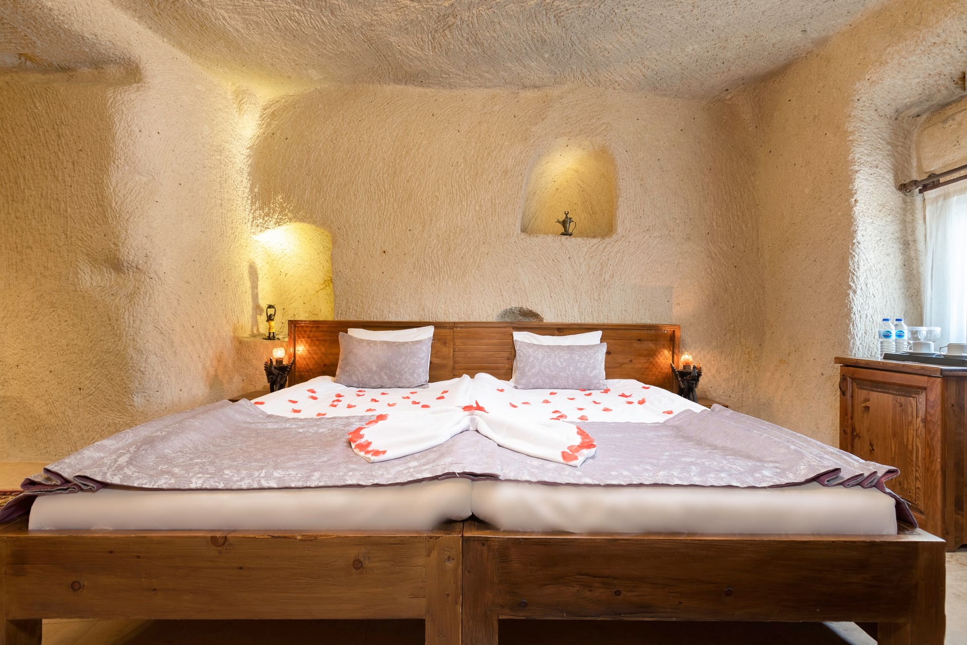 Room 113, Junior Cave Suite: wooden dresser at the foot of the bed, scattered rose petals, rug