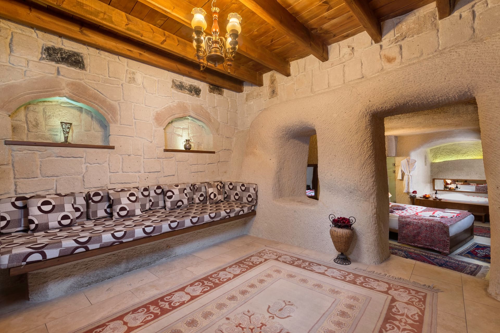 Room 111, King Cave Suite: the patterned bench under the beamed, chandeliered ceiling, wall niches with a vase and ornament, passage to the bedroom