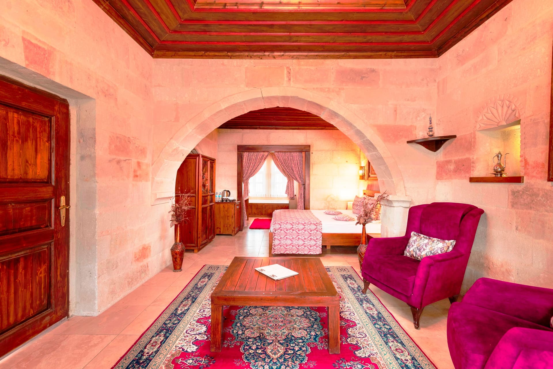 Room 105, King Suite: view through the stone archway toward the seating corner with purple armchairs and a wooden table