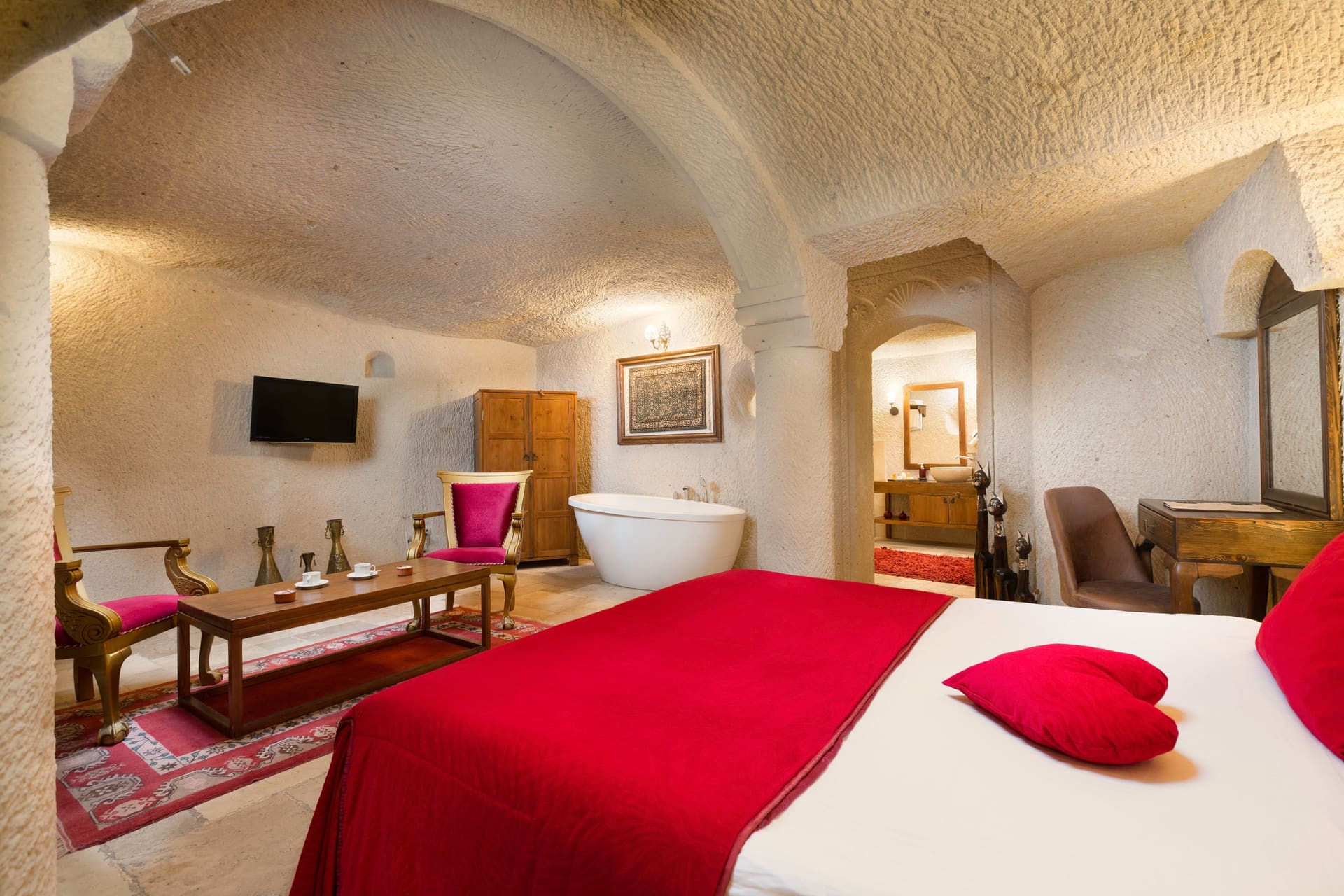 Room 115, Junior Cave Suite: bed, bathtub, wall-mounted TV and mirror, burgundy chairs