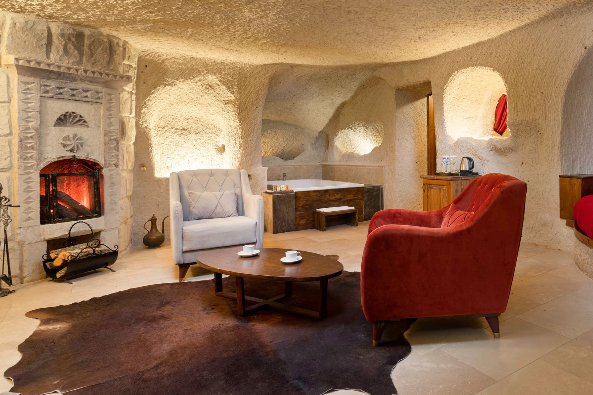 Room 106, King Cave Suite: fireplace and armchairs in the foreground, the red-covered bed visible in the background