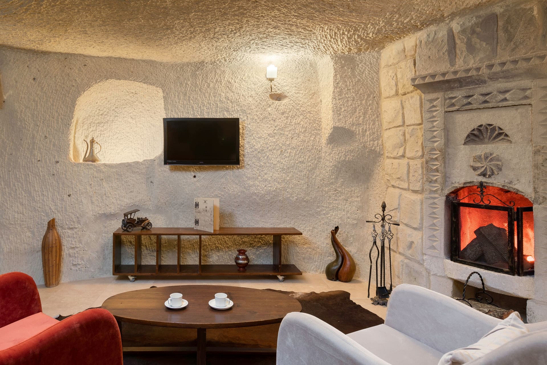 Room 106, King Cave Suite: wall-mounted TV and the lit fireplace seen from a closer angle, armchairs in the foreground