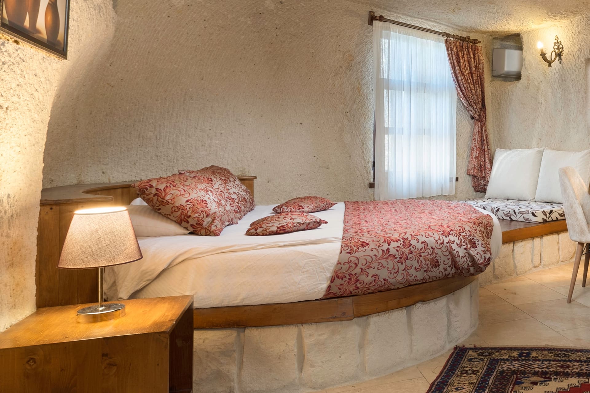 Room 112, King Cave Suite: close view of the bed, a window with sheer curtains, and the adjoining bench seat