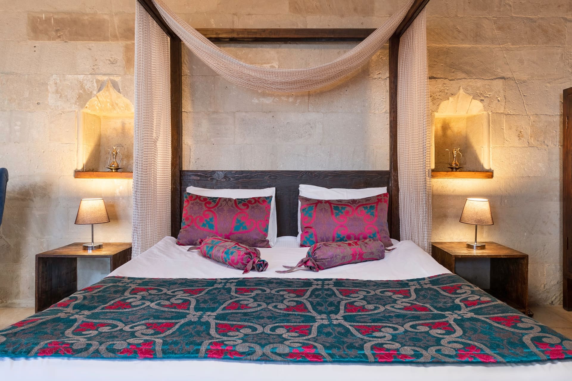 Room 102, Junior Suite: Canopy bed posts, patterned bedspread, stone wall in background.