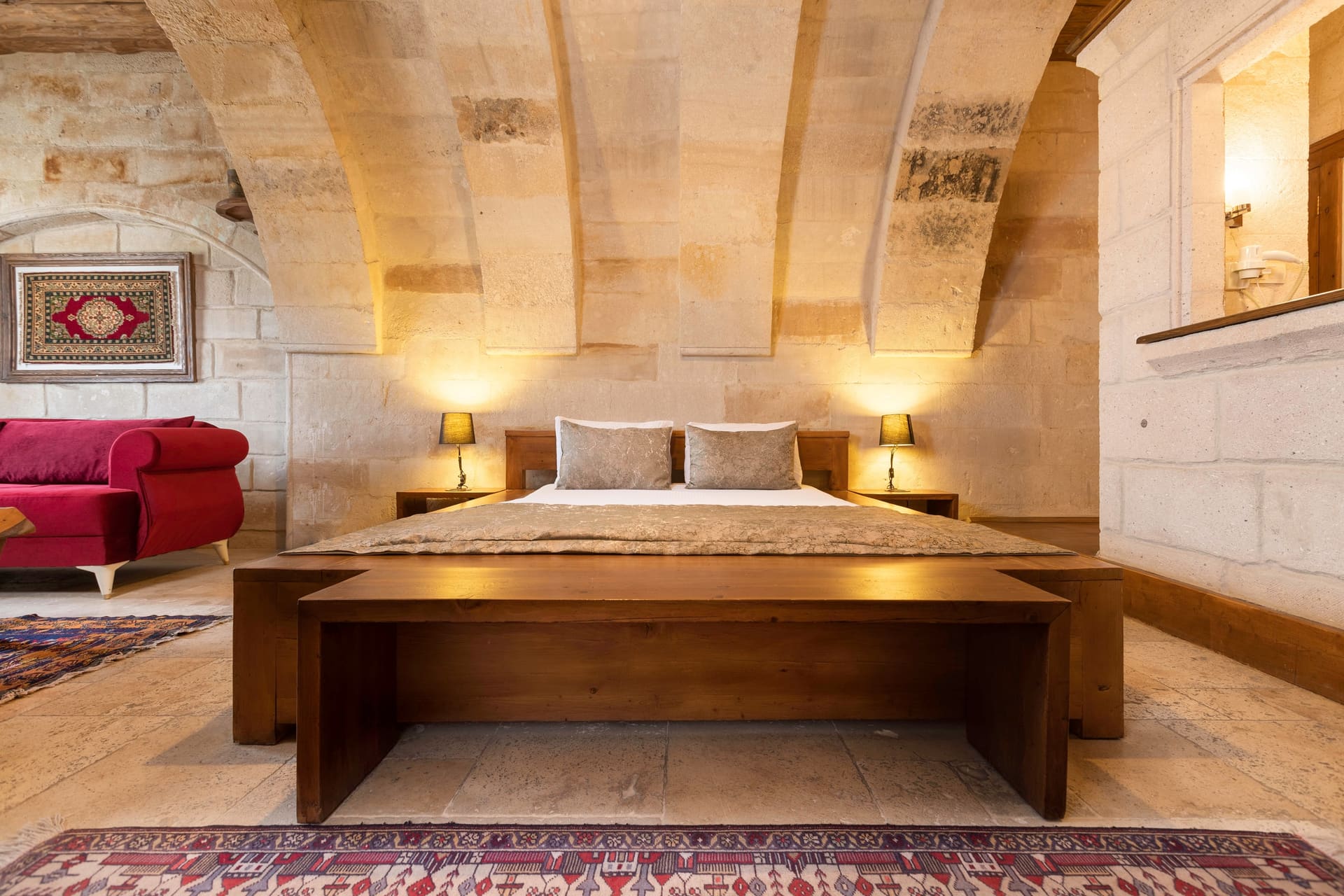 Room 108, Junior Suite: Wide bed, wood-plank base, arched stone wall, lamp on each side.