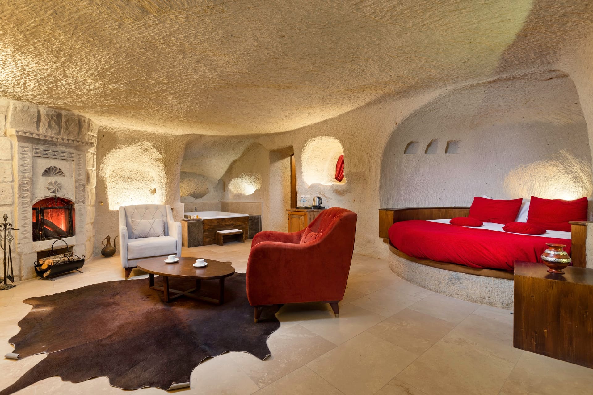 Room 106, King Cave Suite: wide view of the lounge area with a lit fireplace, white and rust armchairs, a round table