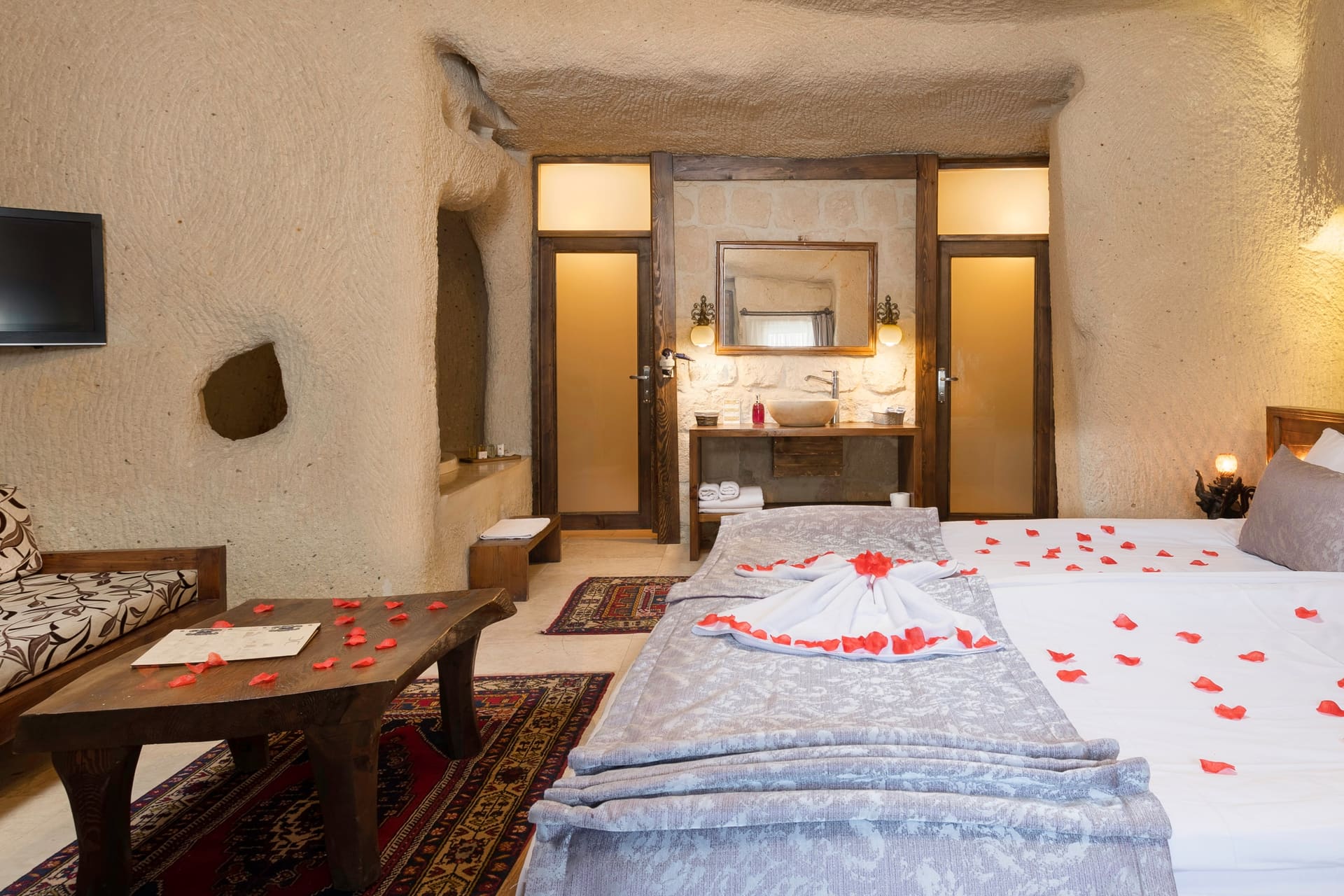 Room 113, Junior Cave Suite: bedside table with a candle, small wall TV, rose petals on the bed