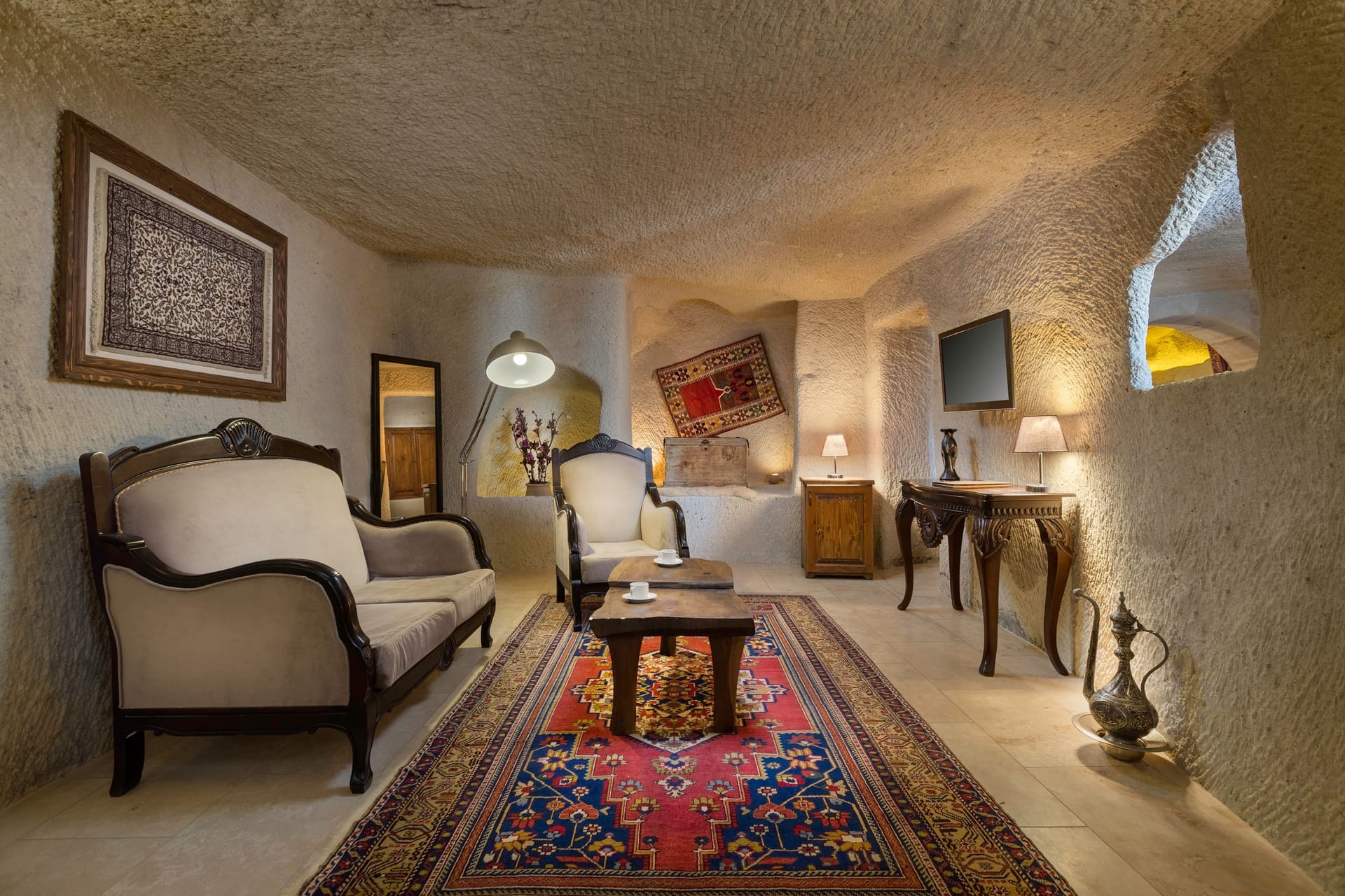 Room 112, King Cave Suite: wide view of the sitting room with a sofa, armchair, wall carpet, console table and TV