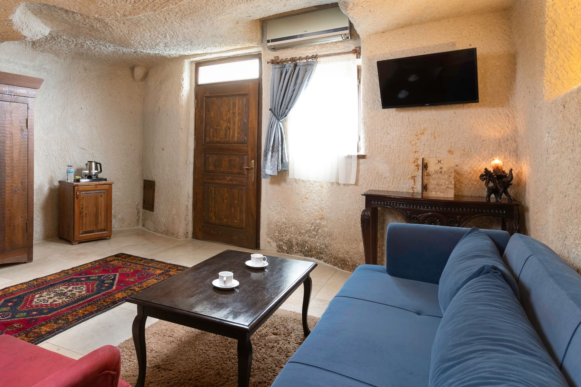 Room 114, Junior Cave Suite: entrance area, wardrobe, air conditioner, wall TV, blue sofa
