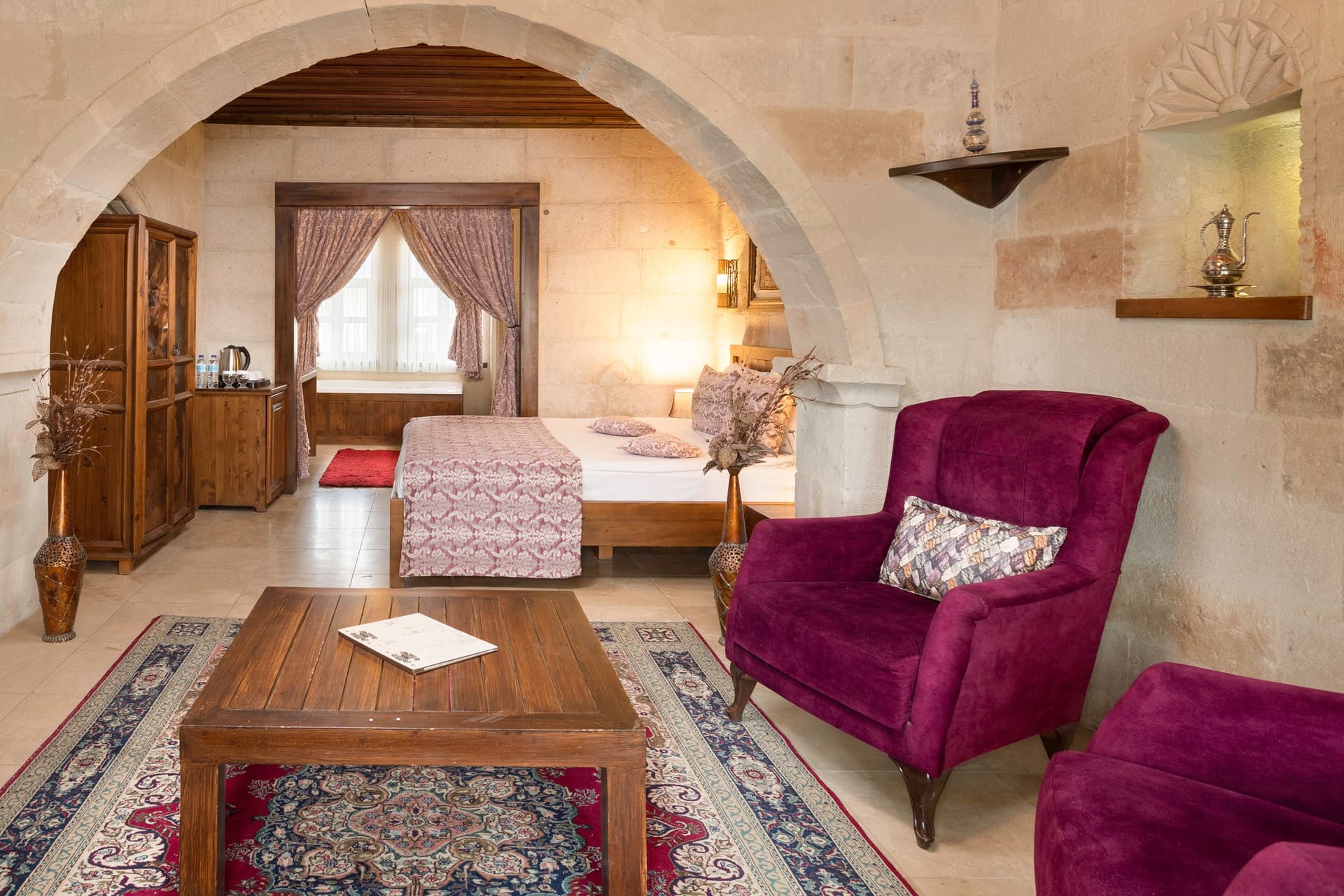 Room 105, King Suite: view through the arch into the bedroom with a wooden wardrobe, bed and purple armchair