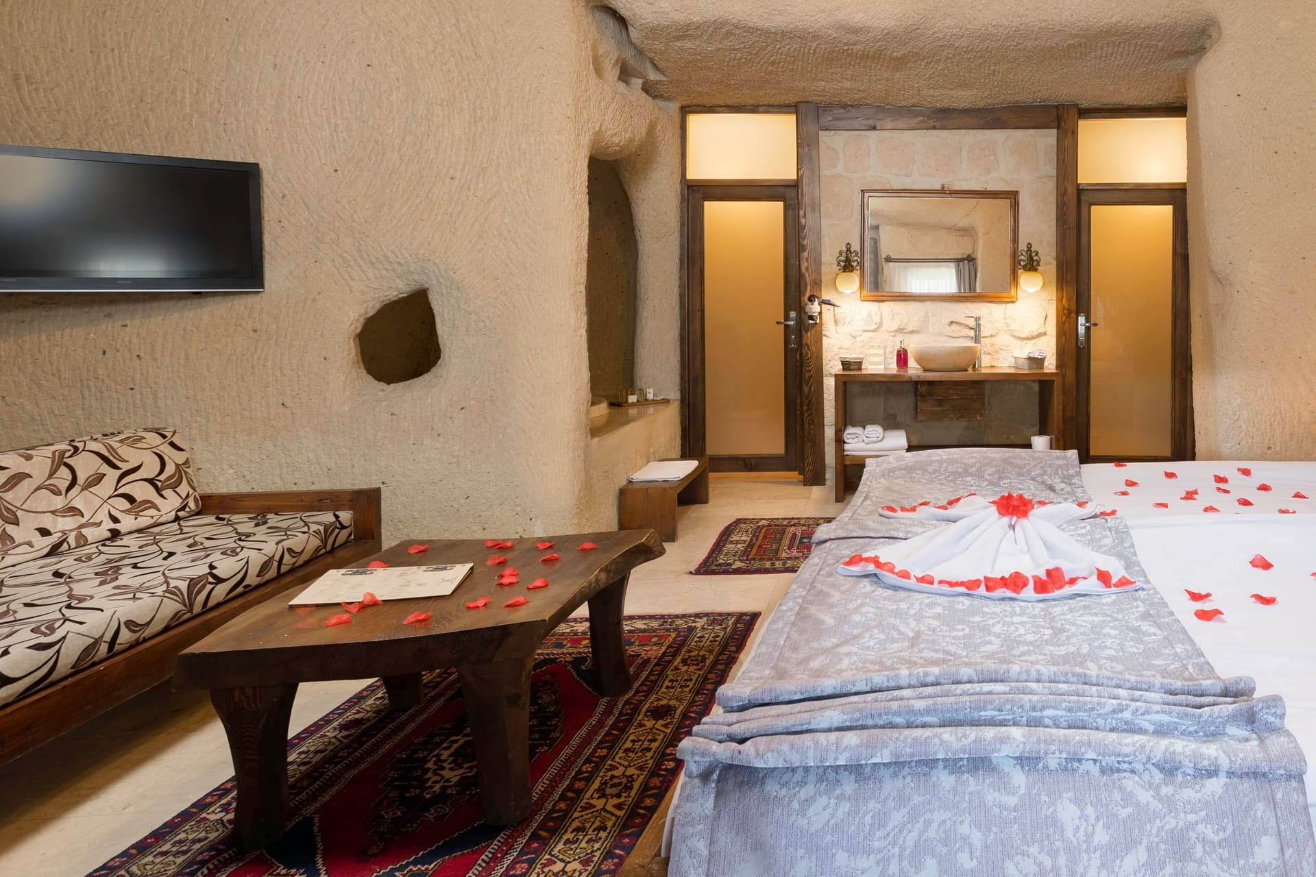 Room 113, Junior Cave Suite: bed and mirrored console, bench seat, scattered rose petals on the bedspread