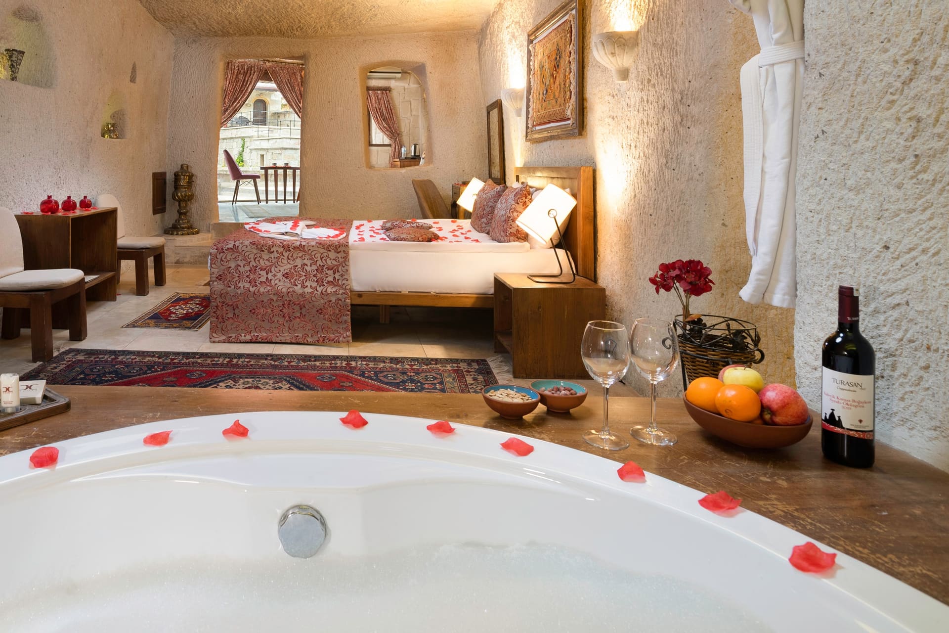 Room 111, King Cave Suite: the jacuzzi tub in the foreground, the bed behind it, wine and a fruit bowl on the ledge