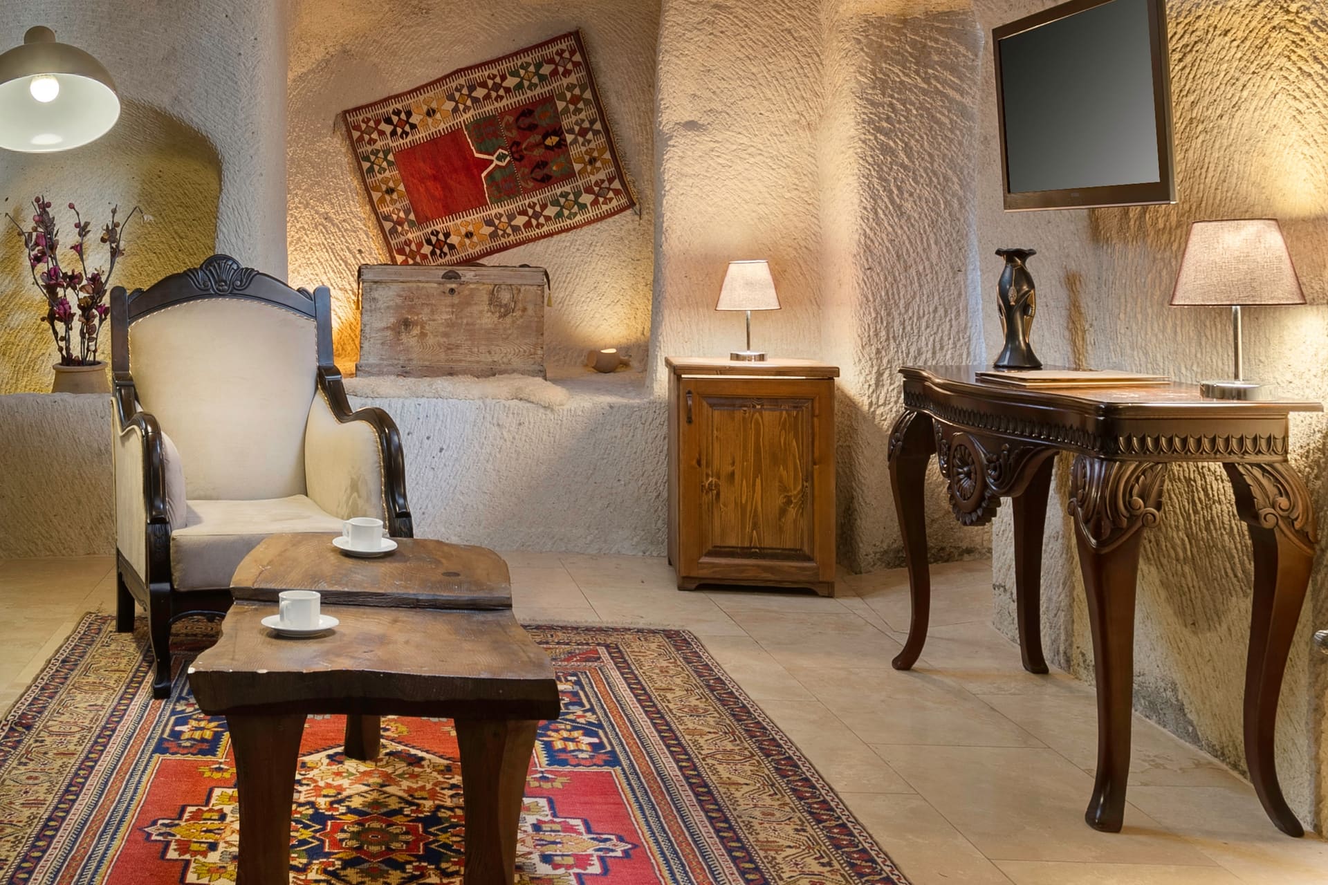 Room 112, King Cave Suite: a single armchair, a wooden trunk, a console table with a TV, and two lamps