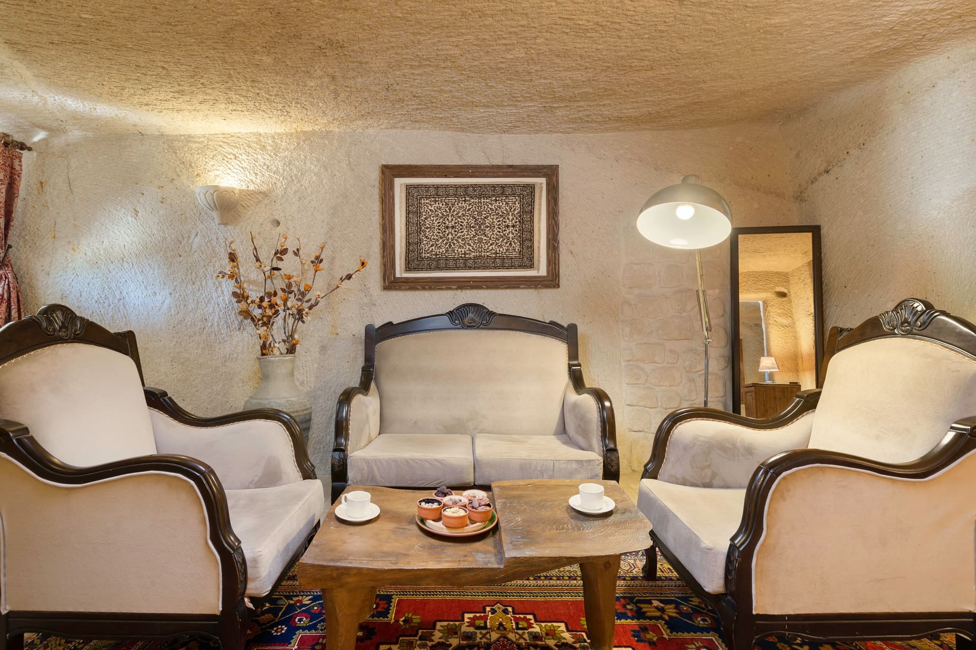 Room 112, King Cave Suite: an antique-style loveseat and two armchairs, a coffee table between them, a woven rug artwork on the wall