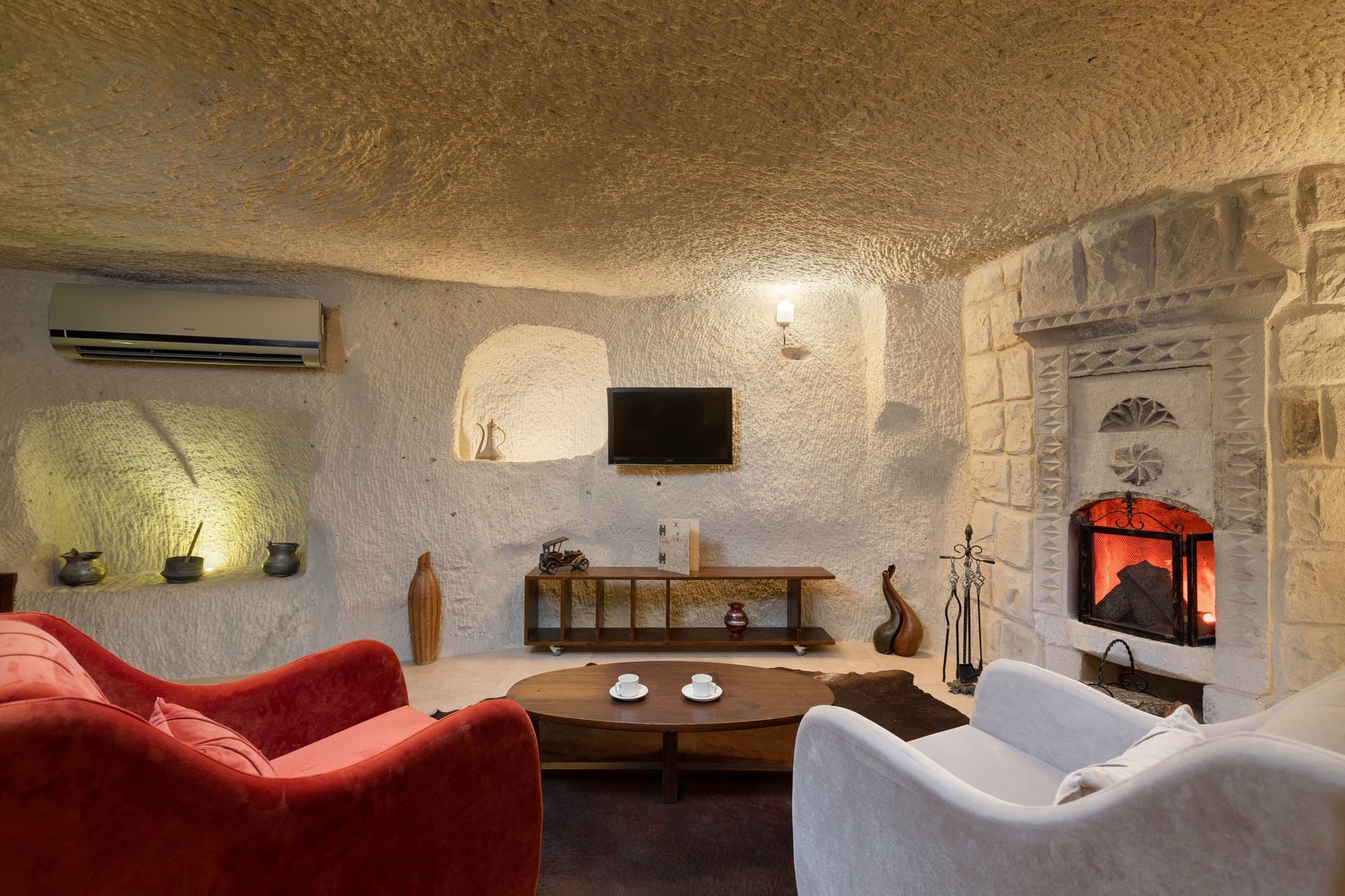 Room 106, King Cave Suite: wall-mounted air conditioner and TV console, ornaments on a niche shelf, the lit fireplace to the right