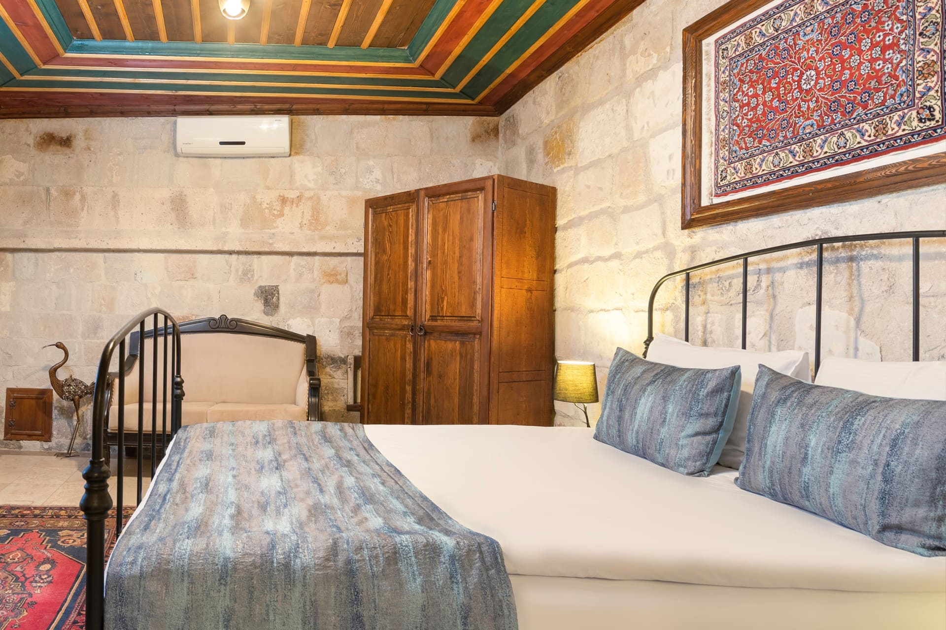 Room 101, Deluxe: Double bed with blue-gray patterned bedspread and pillows, wooden wardrobe
