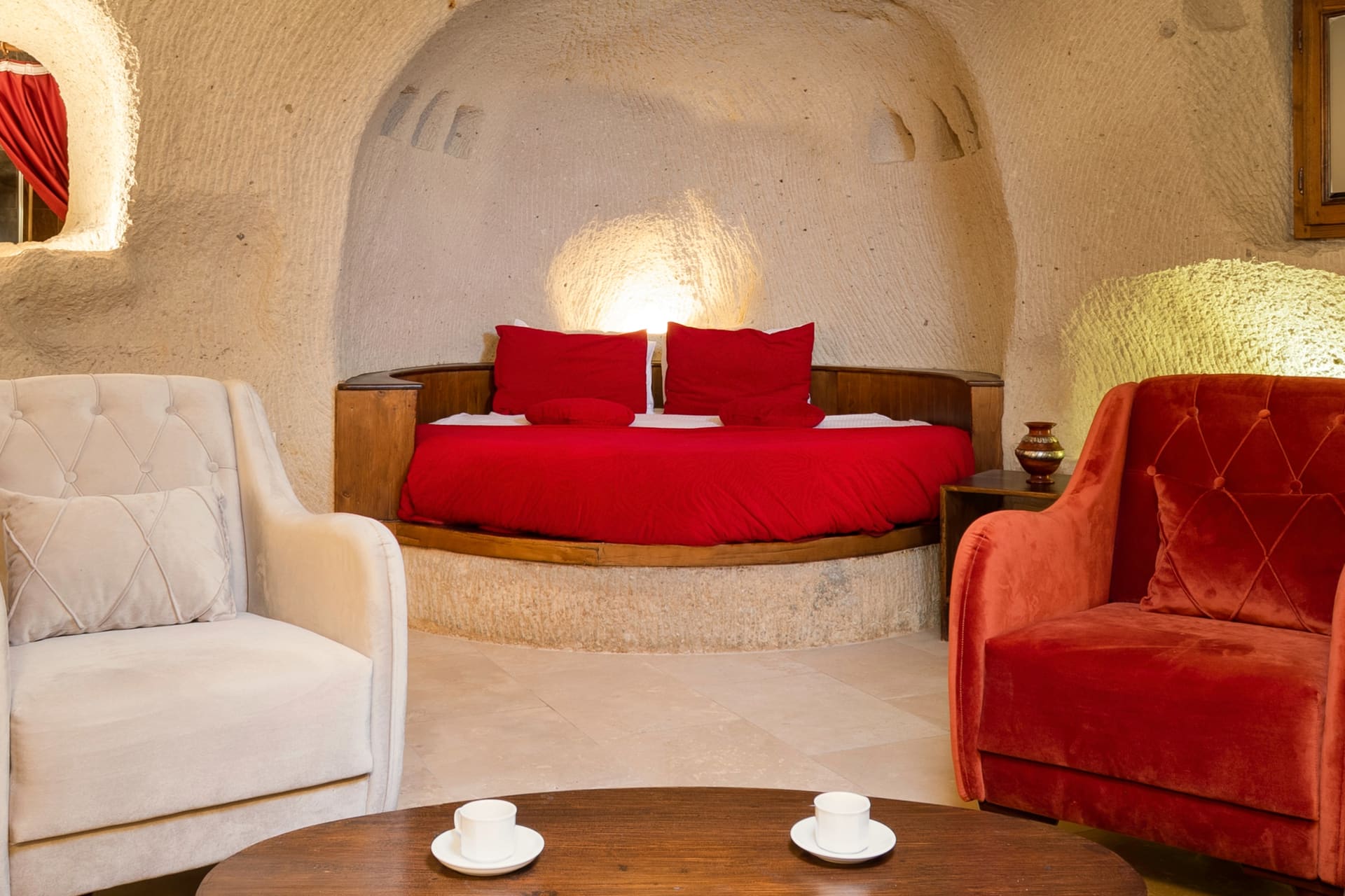 Room 106, King Cave Suite: close view of the red-covered bed, two armchairs, and coffee cups on the table